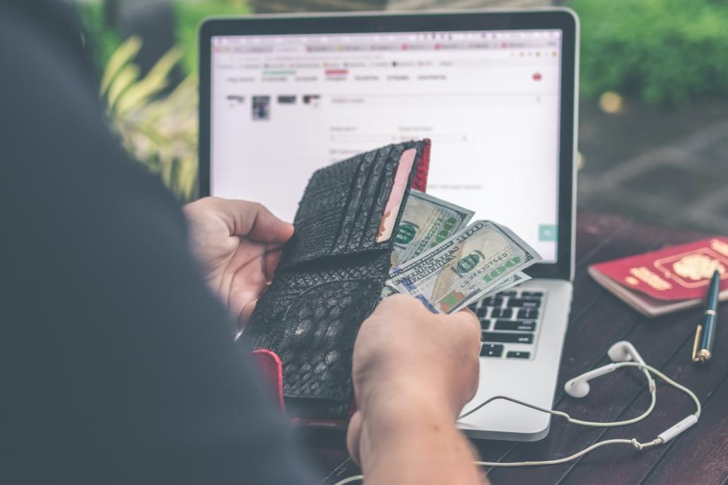 Person holding 100 U.S. dollar bill in front of laptop